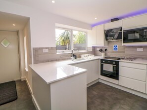 A modern kitchen with a central island, built-in oven, microwave, and a window providing natural light. - Baytree House (Sheffield)