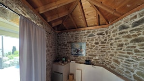 Une pièce aux murs de pierre et au plafond en bois, avec une petite table, une bouilloire, une poubelle et un tableau accroché au mur.