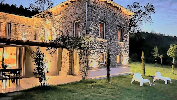 Une maison en pierre avec un balcon, une pelouse avec des chaises longues et une table.