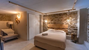 Une chambre avec un mur en pierre, un lit, une table de chevet, une lampe et une chaise.