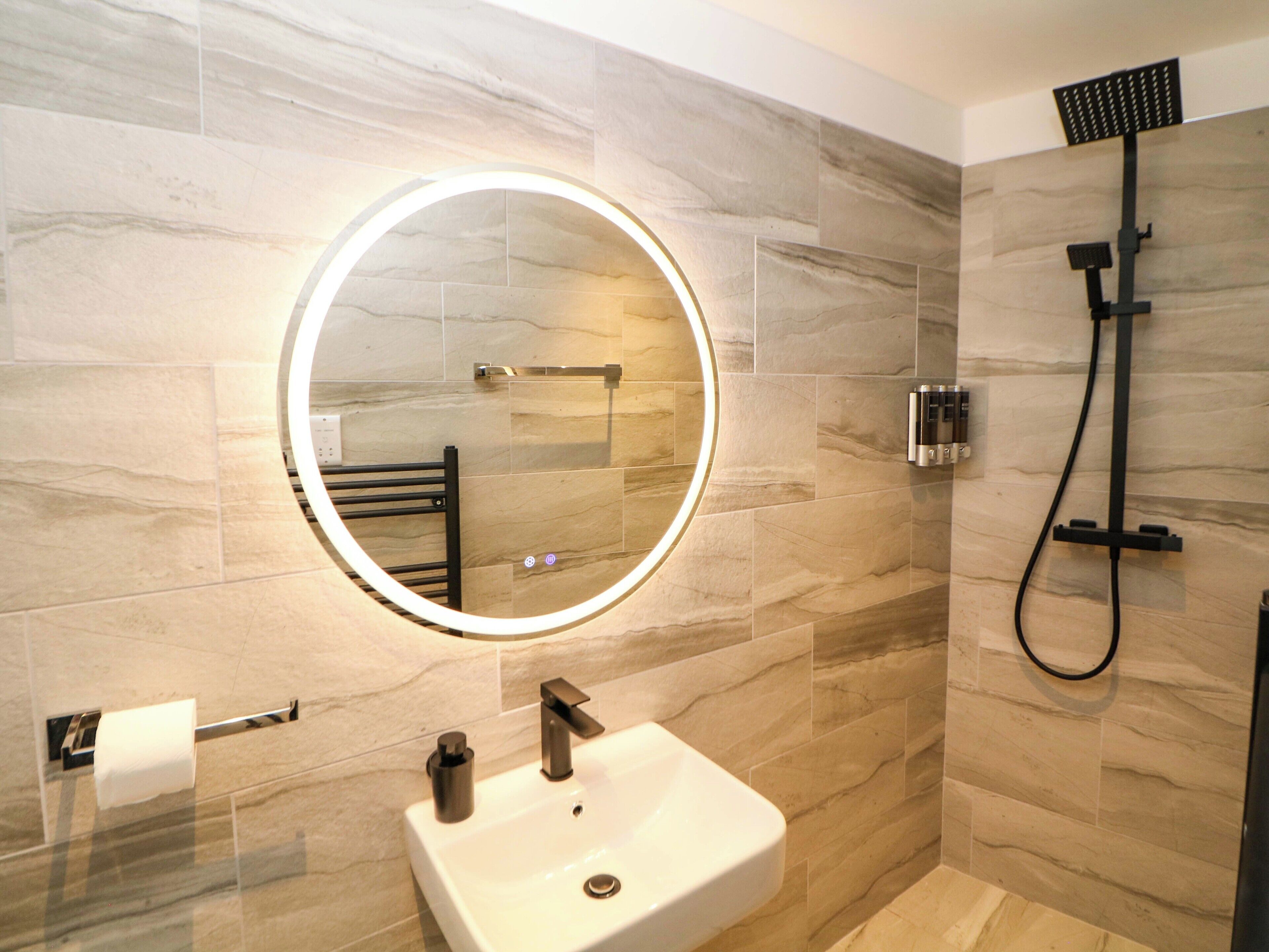 A bathroom with a round mirror, a sink, a handheld showerhead, and a towel rack.