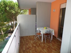 Ein Balkon mit Tisch und Stühlen, Blick auf Bäume und ein Gebäude im Hintergrund.