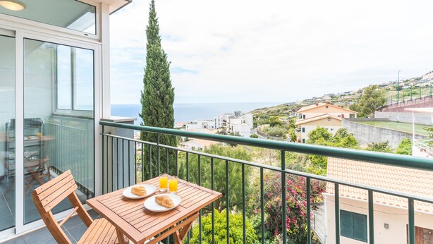 Ein Balkon mit Tisch, Stühlen und Blick auf das Meer und Gebäude.