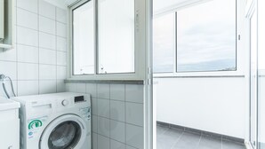 Ein kleiner Waschraum mit einer Waschmaschine mit Frontlader, einem Fenster und Fliesenboden.