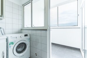 Ein kleiner Waschraum mit einer Waschmaschine mit Frontlader, einem Fenster und Fliesenboden.