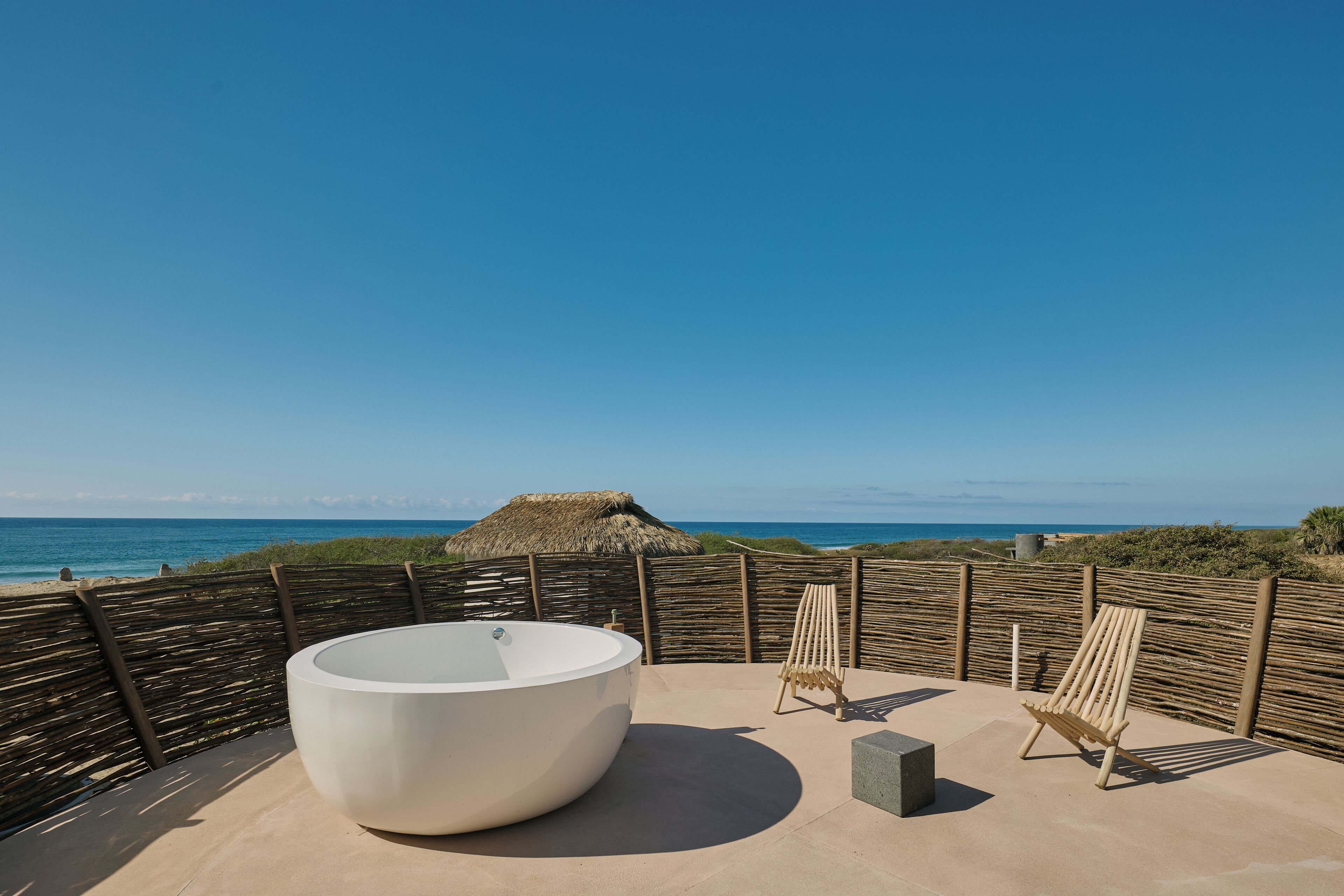 A rooftop with a large bathtub, two lounge chairs, and a view of the ocean.