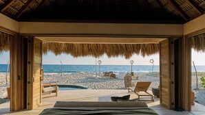Habitación frente a la playa con techo de paja, paredes de madera y vista al mar.