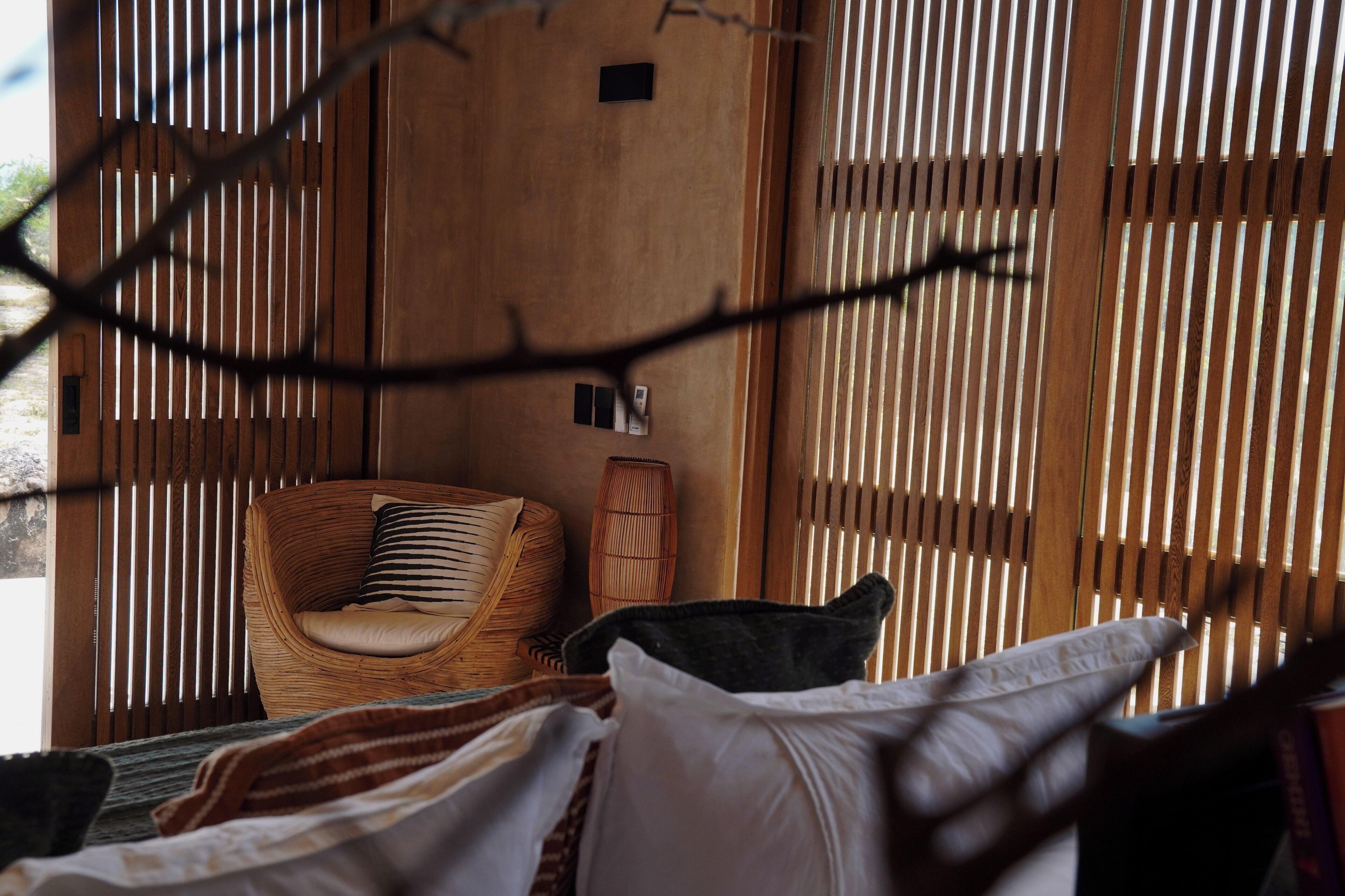A room with a bed, a wicker chair, and a window with vertical blinds.