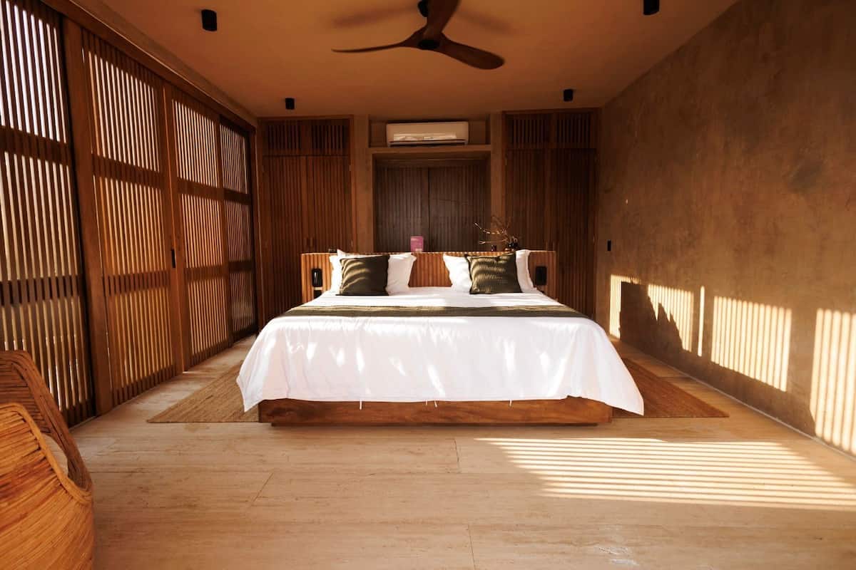 Un dormitorio con una cama grande, paredes de madera, un ventilador de techo y una ventana que deja entrar luz natural.