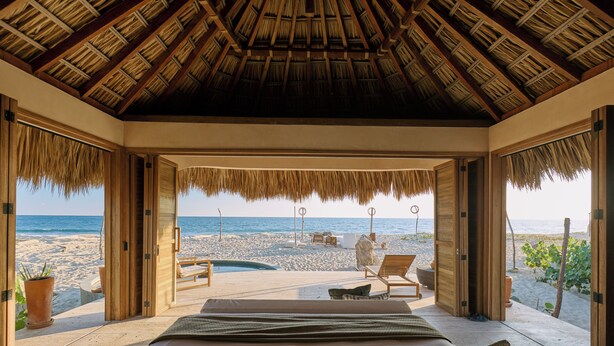 Habitación frente a la playa con techo de paja, una cama, vistas a la playa y una pequeña piscina.