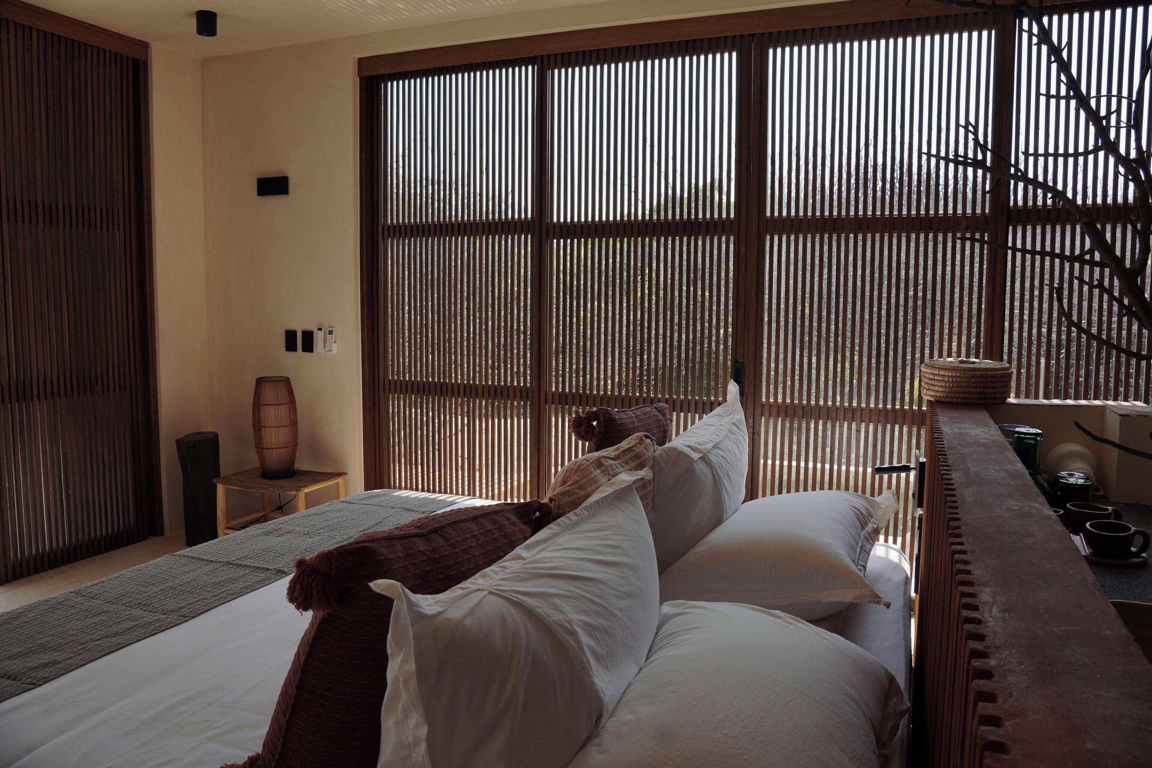 A room with a bed, a small table, and a window with vertical blinds.