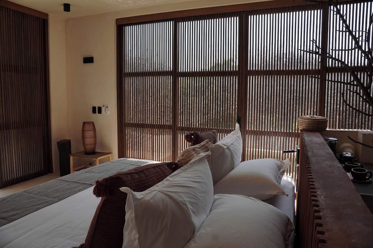 Una habitación con cama, una mesita y una ventana con persianas verticales.
