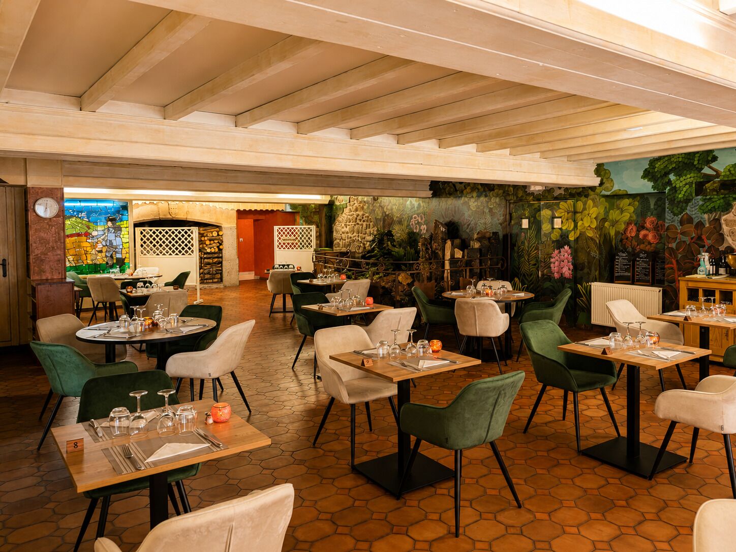 Ein Restaurantinnenraum mit sechseckigem Fliesenboden, grünen Sitzstühlen und gedeckten Tischen.