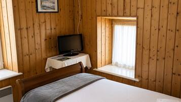 A wooden-paneled room with a bed, a desk, a television, and a window with curtains.
