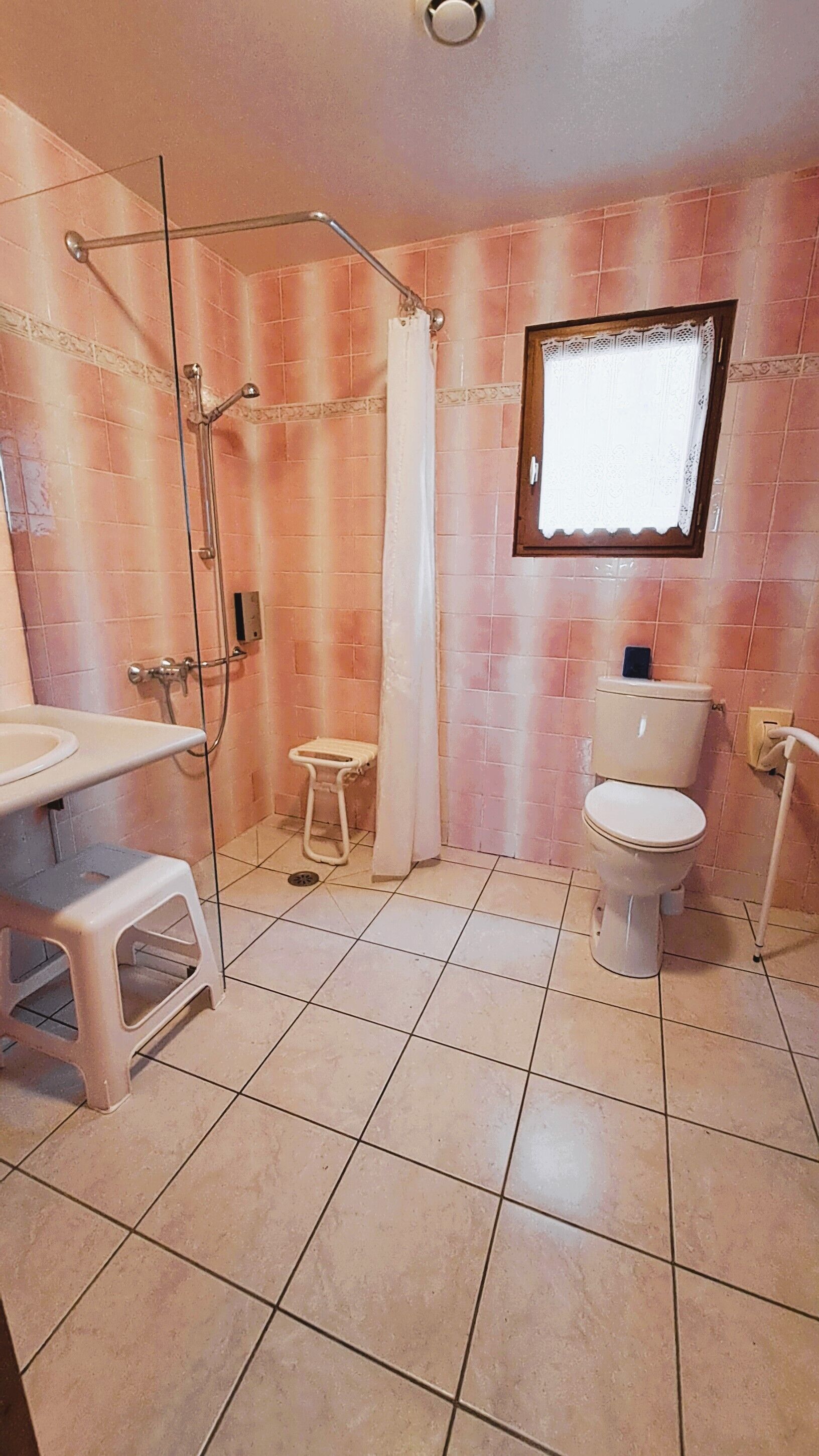 A bathroom with a shower, toilet, sink, and a small stool.