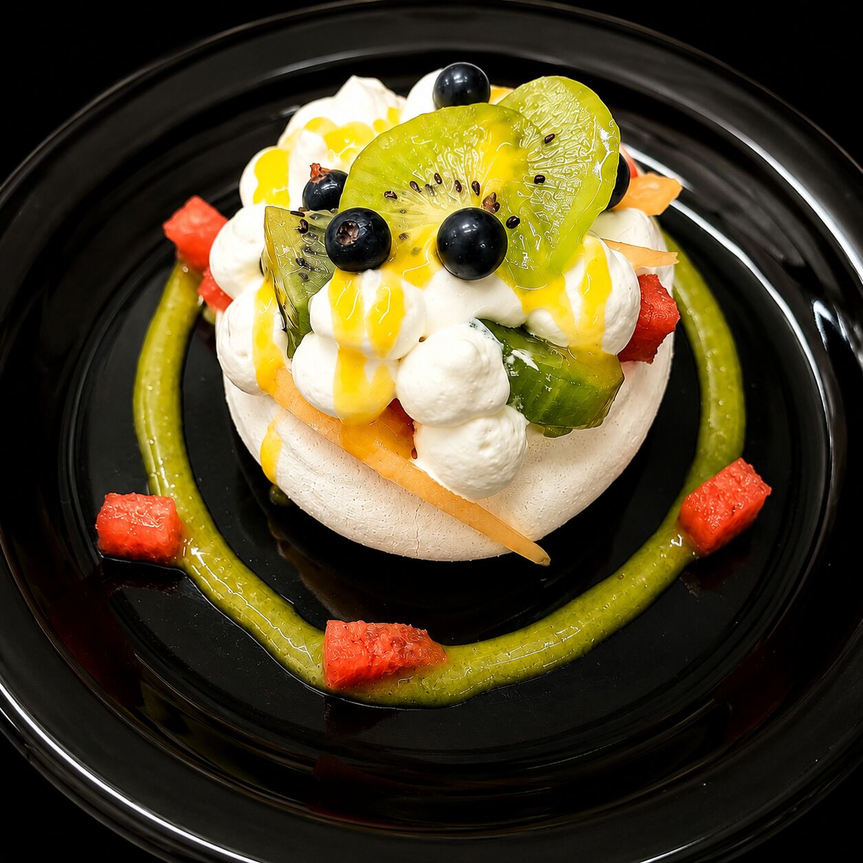 A dessert on a black plate with meringue, kiwi, blueberries, and a green sauce.