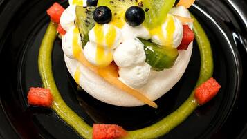 A dessert on a black plate with meringue, kiwi, blueberries, and a green sauce.