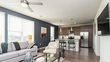 A modern living room with a sofa, a coffee table, and a kitchen area with a refrigerator, microwave, and bar stools.