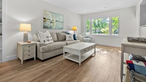 A modern living room with a sofa, two side tables with lamps, a coffee table, and a large window with a view of greenery.