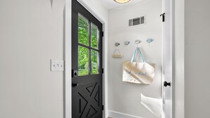 A black door with geometric patterns, a white wall with a 'LAKE HOUSE' sign, and a beige bag hanging on a hook.