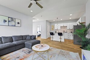 A modern living room with a grey sofa, a small round table, and a colorful rug. - Modern 4BR | Chef`s Kitchen + Soaking Tub · Indy (Indianapolis)