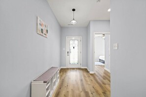 A hallway with a bench, a door with a glass panel, and a light fixture. - Modern 4BR | Chef`s Kitchen + Soaking Tub · Indy (Indianapolis)