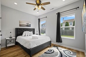 A bedroom with a bed, a ceiling fan, a nightstand, a window with curtains, and a view of the outside. - Modern 4BR | Chef`s Kitchen + Soaking Tub · Indy (Indianapolis)