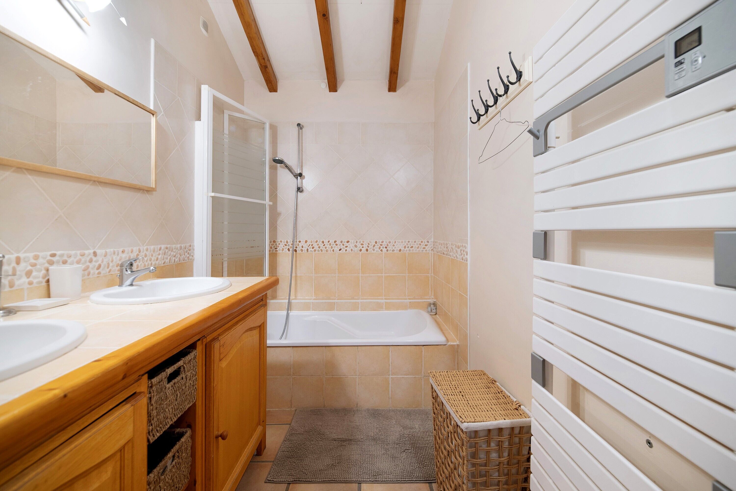 A bathroom with two sinks, a bathtub, wooden cabinets, a woven basket, and a towel rack.