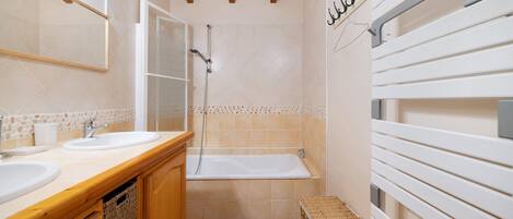 A bathroom with two sinks, a bathtub, wooden cabinets, a woven basket, and a towel rack.