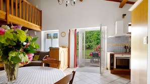 Een eetgedeelte met een ronde tafel, stoelen, een vaas met bloemen, een houten trap en een keuken met een fornuis.