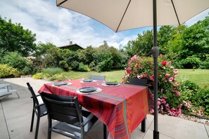 Patio esterno con tavolo apparecchiato per quattro persone, circondato da sedie e riparato da un ombrellone grande.
