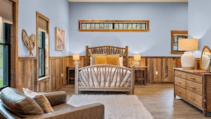 Un dormitorio con una cama y un aparador de madera, un sofá, y un ventanal con persianas.