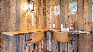 Una barra de madera rústica con dos taburetes de cuero, un cartel antiguo y una lámpara de pared.