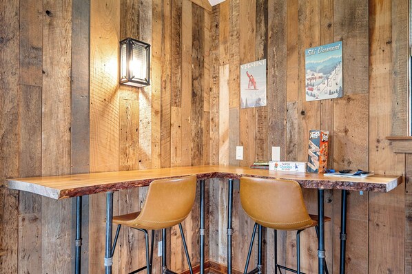 A rustic wooden bar with two leather barstools, a vintage poster, and a wall-mounted light fixture.