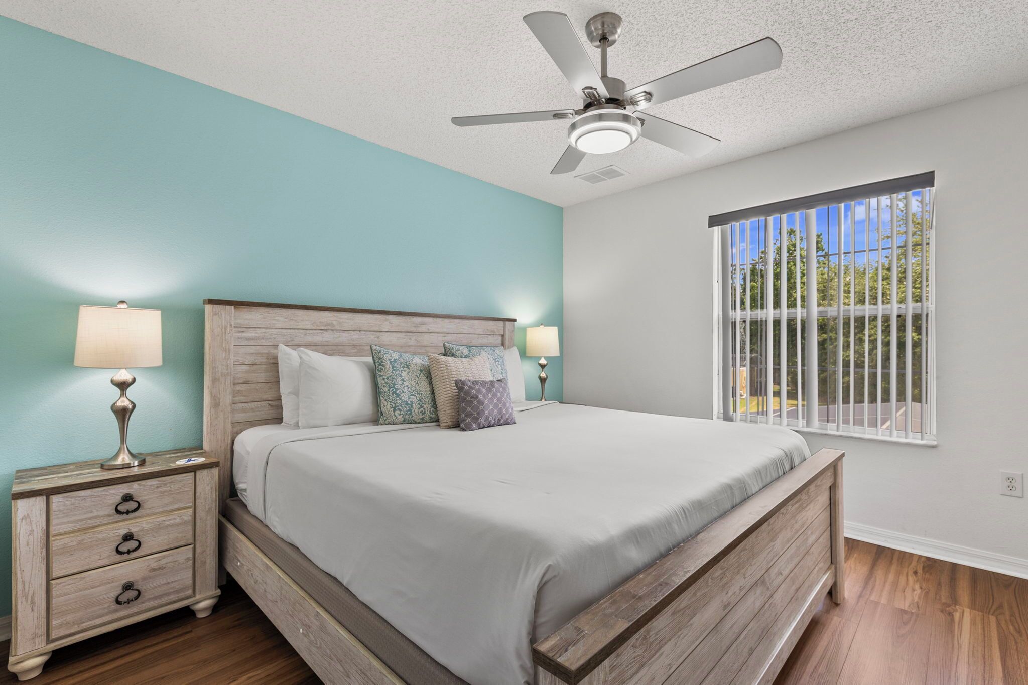 A bedroom with a bed, nightstands, a ceiling fan, and a window with a view.