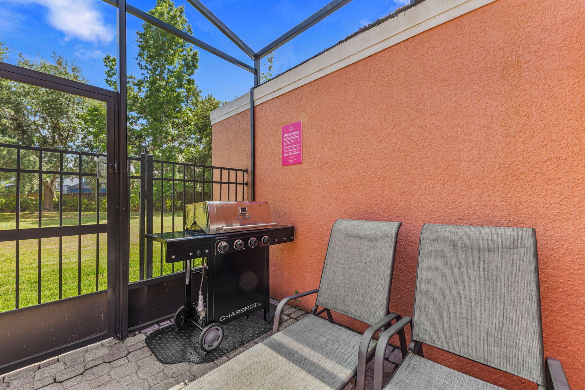 A patio area with a grill, two chairs, a glass door, and a wall with a sign.