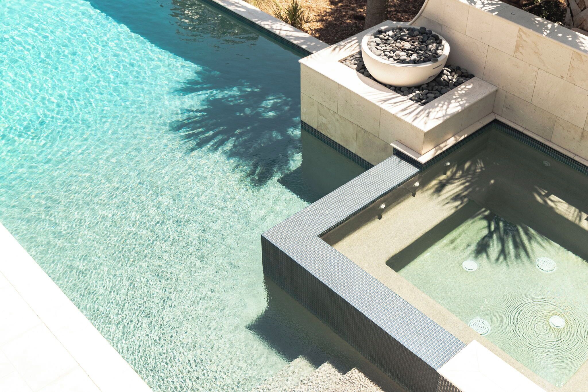 A clear swimming pool with a tiled edge, a built-in planter with rocks, and a stone wall.