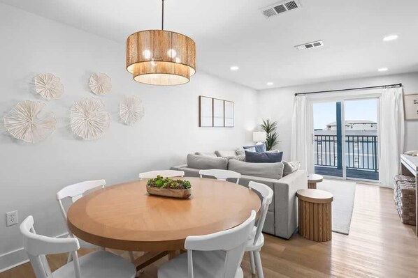A modern living room with a round wooden table, white chairs, a grey sofa, and a large window with a view. - Snowbird Rates Beachfront Bliss 3 bedroom sleeps 8 (Gulf Shores)