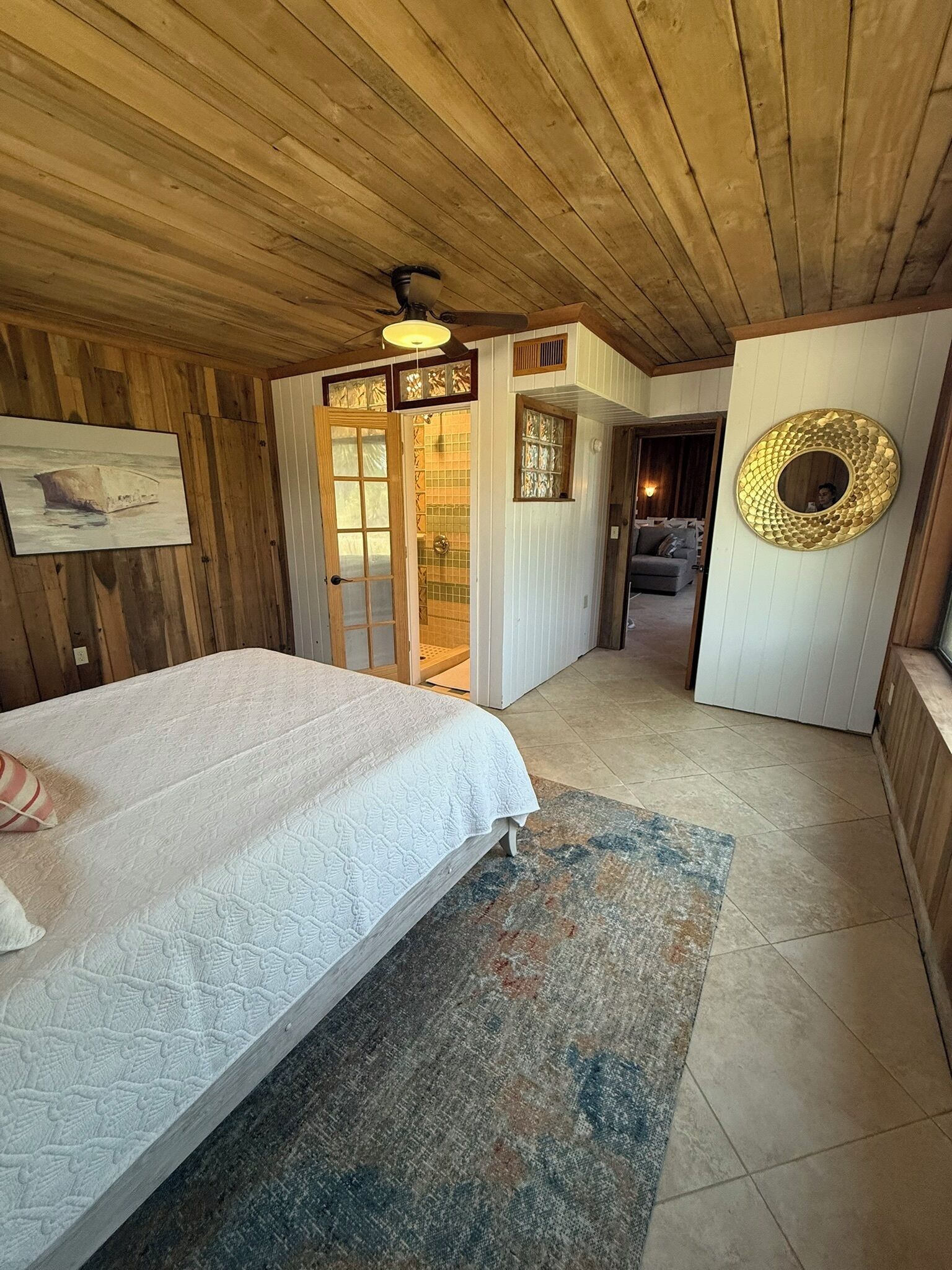 Une chambre à coucher avec un lit, un plafond en bois, une porte donnant sur une salle de bain et un miroir rond accroché au mur.