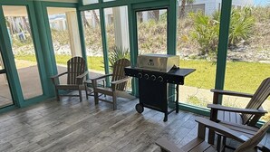 Eine überdachte Terrasse mit Holzboden, Deckenventilator und Grill.