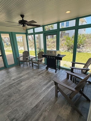 Eine überdachte Terrasse mit Holzboden, Deckenventilator und Grill.