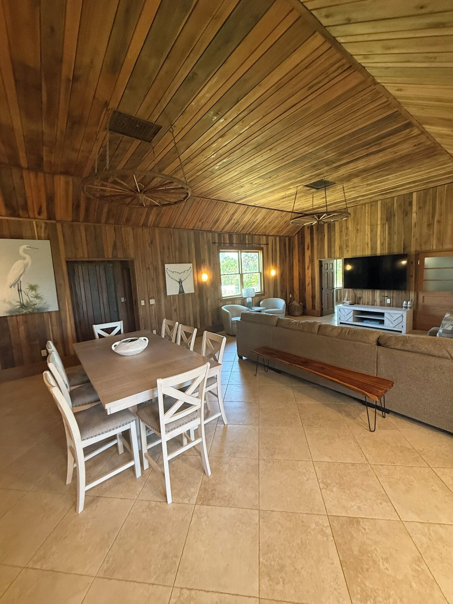 A wooden interior with a dining table, chairs, a bench, a sofa, and a TV.