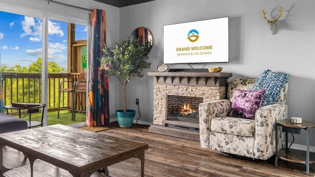 Una sala de estar con chimenea, televisor montado en la pared y vistas al exterior.