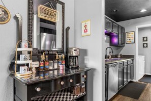 Eine Barbereich mit einer Kaffeemaschine, Regalen für Gewürze, einem Spiegel und einer Neonreklame.