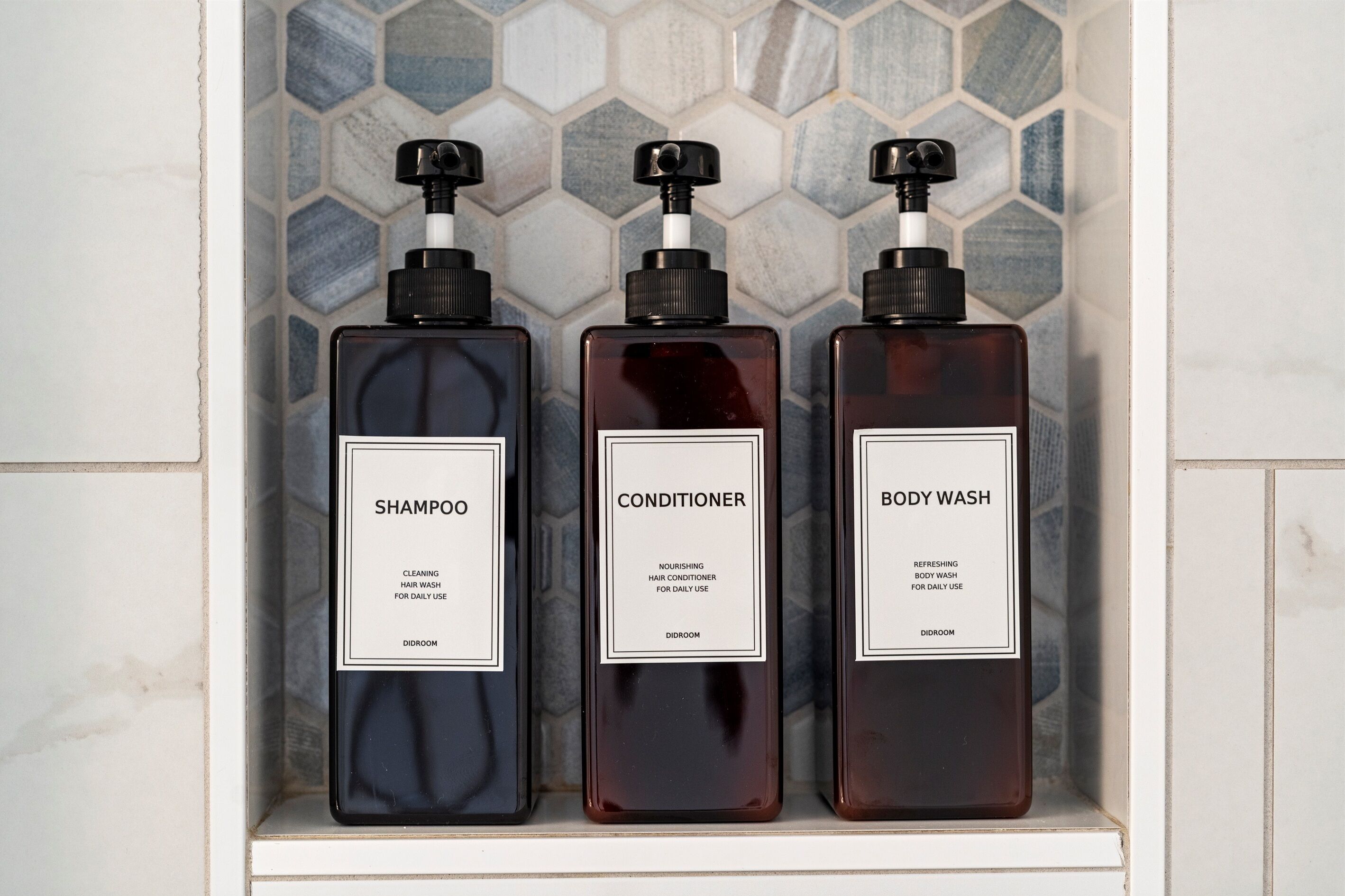 Tres botellas de champú, acondicionador y gel de baño sobre un estante de azulejos.