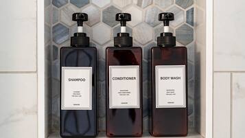 Tres botellas de champú, acondicionador y gel de baño sobre un estante de azulejos.