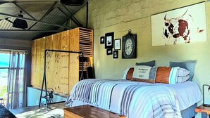 Quarto com cama, um baú de madeira, relógio de parede, quadros emoldurados e uma obra de arte com tema de touro.