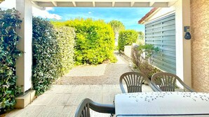 A covered patio with a table and chairs, a gravel path, and a hedge. - Jardin de la Vaunage, Pool & Nature, Sleeps 4 (Calvisson)
