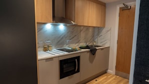 Een compacte keuken met houten kastjes, een ingebouwde oven en een marmeren achterwand.