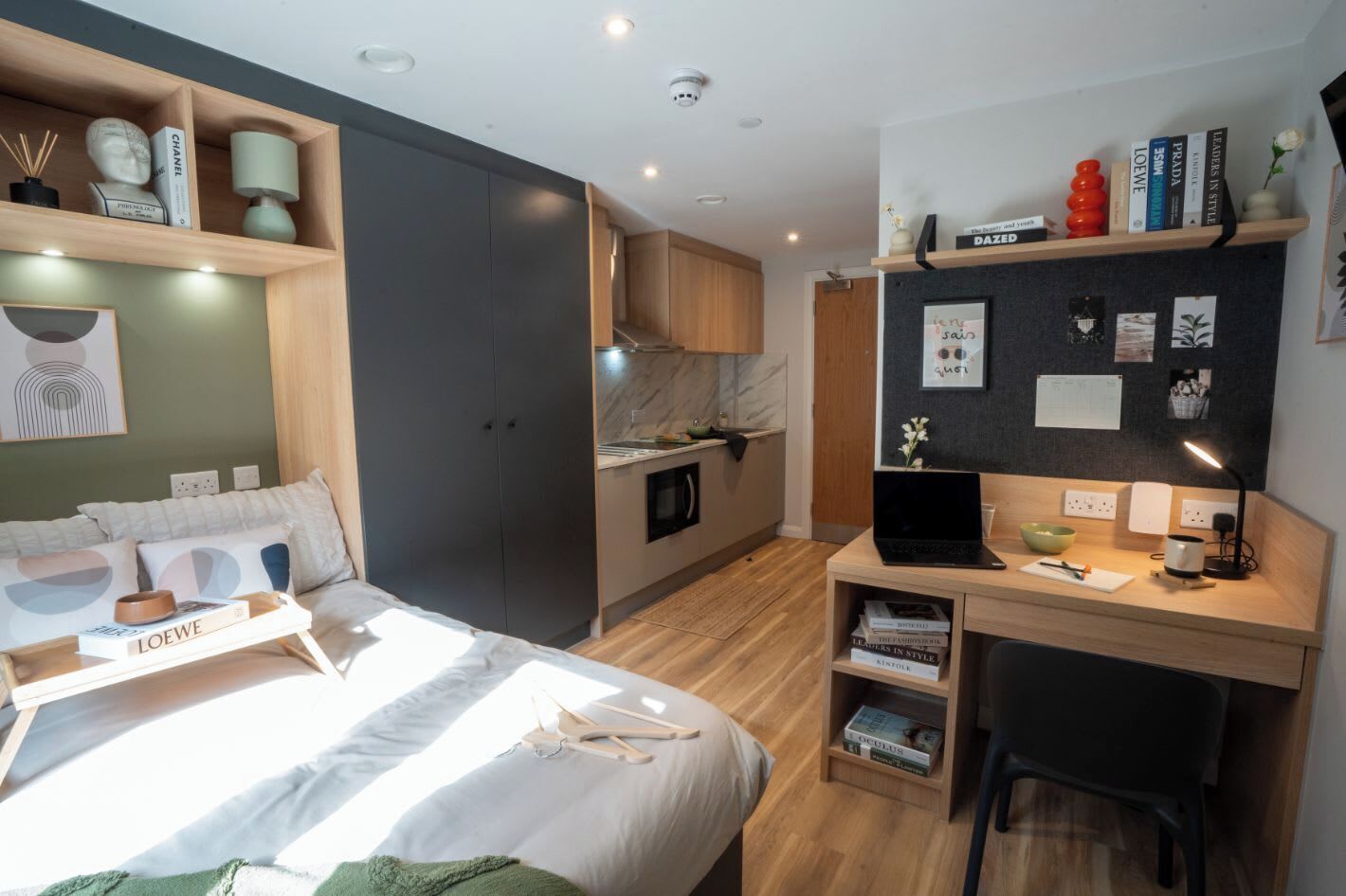 A modern bedroom with a bed, bedside table, and a desk with a laptop.